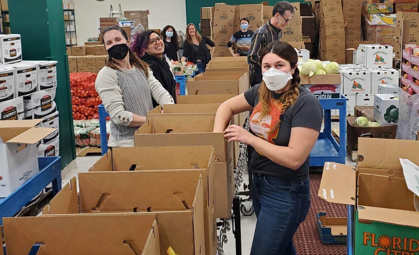 Several people packing food into cardboard boxes.